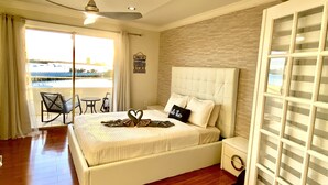 A bedroom with a bed, a nightstand, a chair, a table, a ceiling fan, and a view of the outdoors.