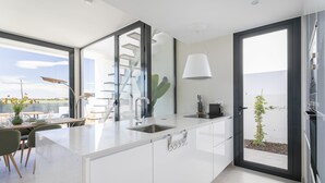 Eine moderne Küche mit weißen Schränken, einem großen Fenster und Blick ins Freie.