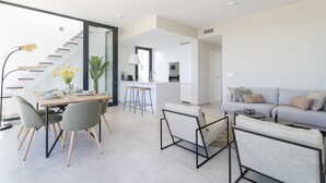 Ein modernes Wohnzimmer mit Sofa, einer Essecke mit Tisch und Stühlen sowie einer Küche im Hintergrund.