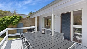 A deck with a table and chairs, a glass door, and a view of the backyard. - Ocean Oasis by Experience Jervis Bay (Vincentia)