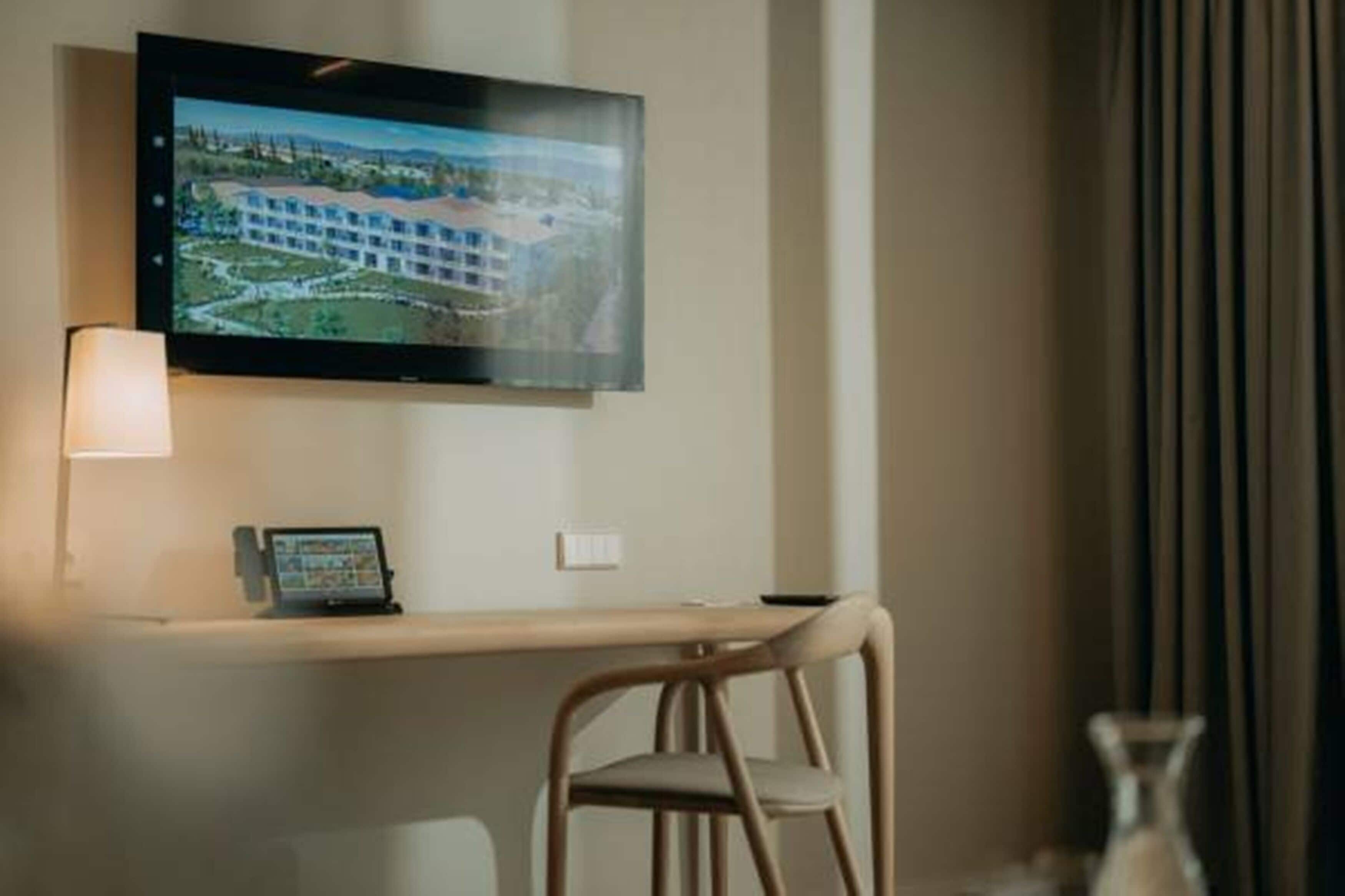 Hotelkamer met een flatscreen televisie aan de muur, een bureau met een laptop en een stoel.