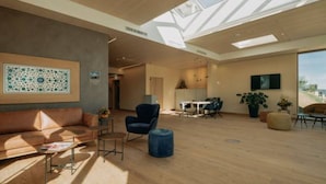 A spacious living area with a high ceiling, skylights, a large window, a sofa, a chair, a table, and a TV. - Landhotel Bohrerhof (Hartheim am Rhein)