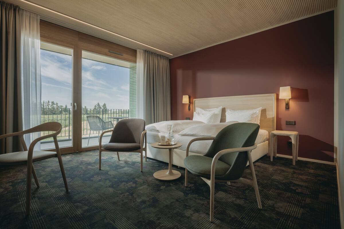 Habitación de hotel con una cama grande, dos sillas, una mesita y vistas al exterior.