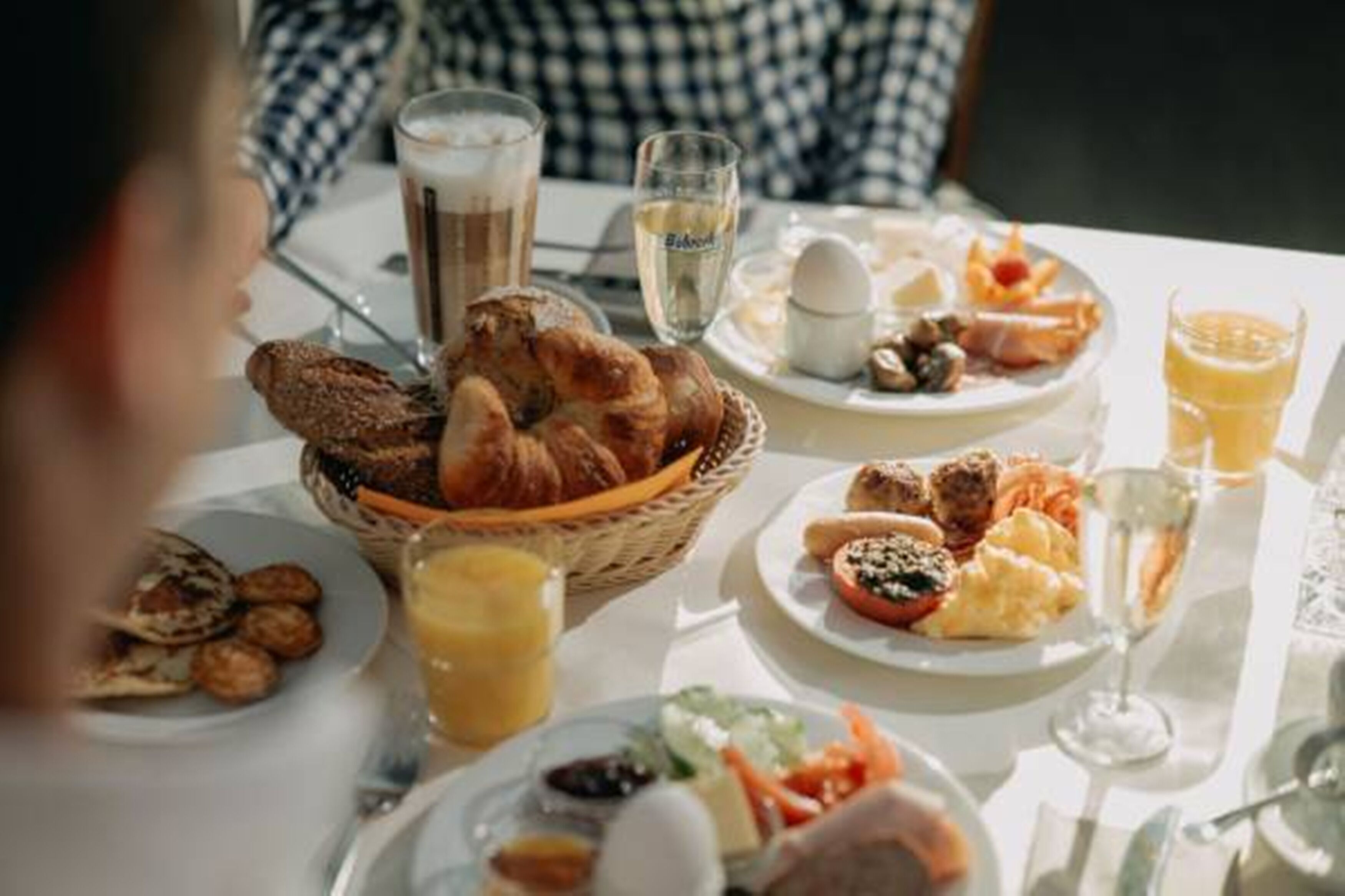 A breakfast setting with croissants, eggs, sausages, and juice on a table.