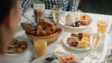 A breakfast setting with croissants, eggs, sausages, and juice on a table.
