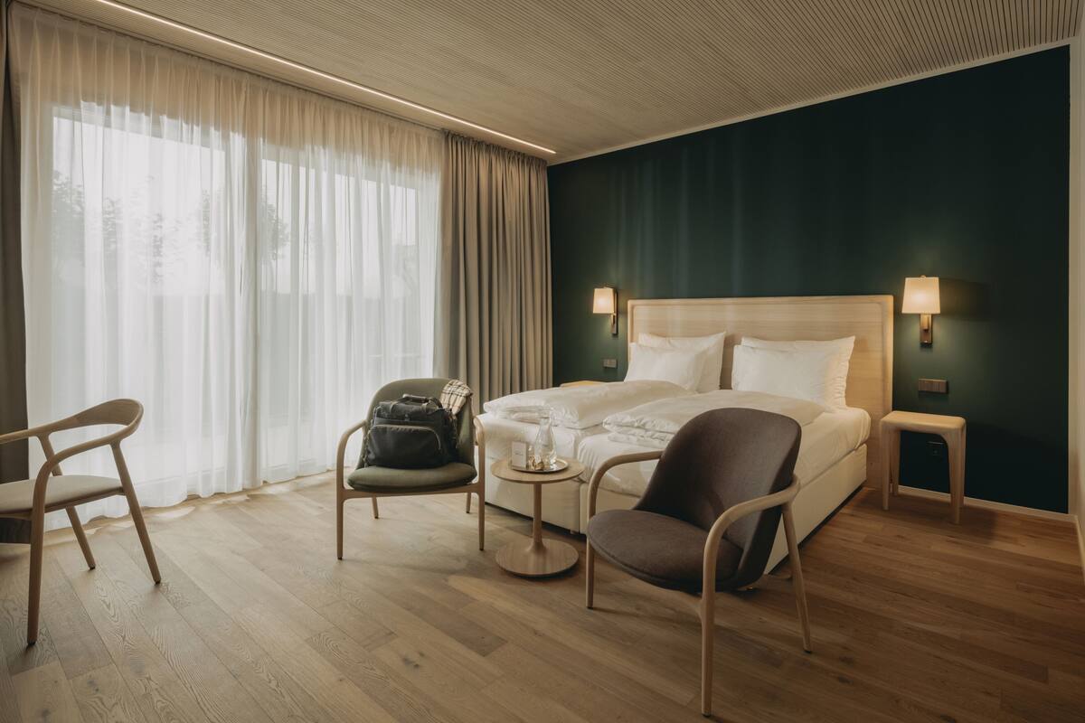 Una habitación de hotel con una cama, dos sillas, una mesita y una mesita de noche con lámparas.