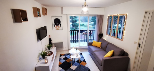 A modern living room with a grey sofa, yellow cushions, a coffee table, and a large window with a view of the outdoors.