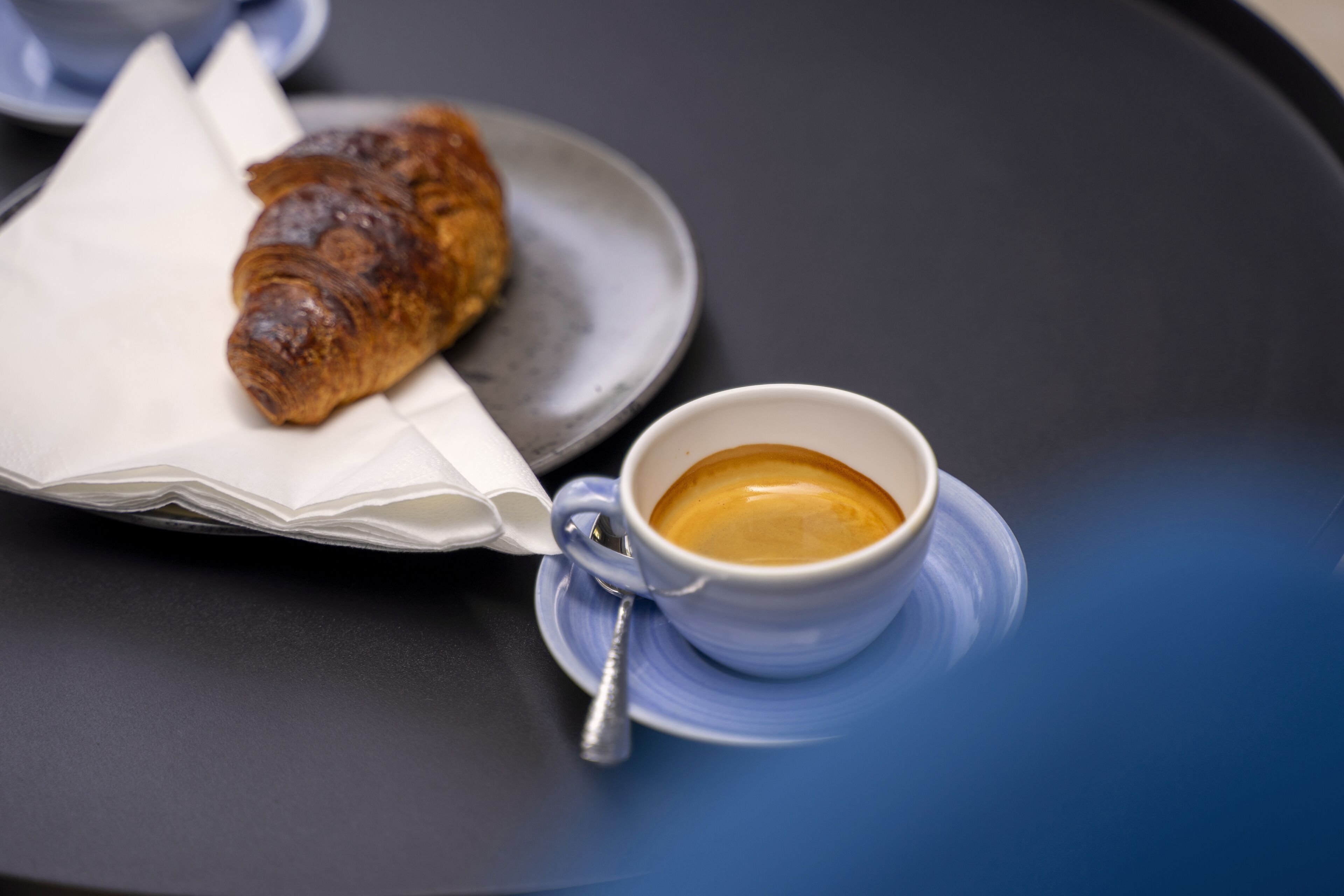 Een croissant op een bord naast een kop koffie op een tafel.