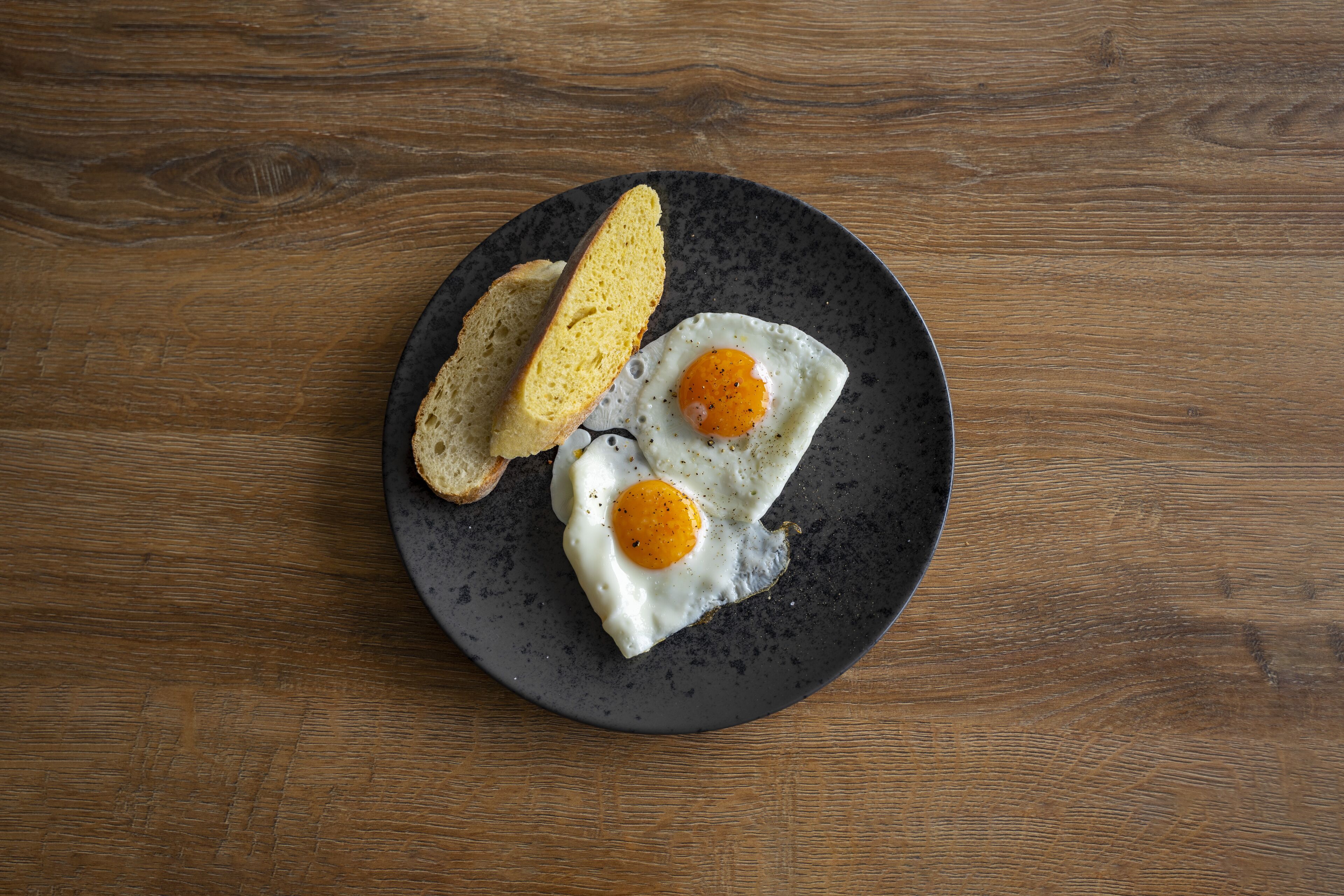 A plate with two fried eggs and two slices of toast on a dark plate.
