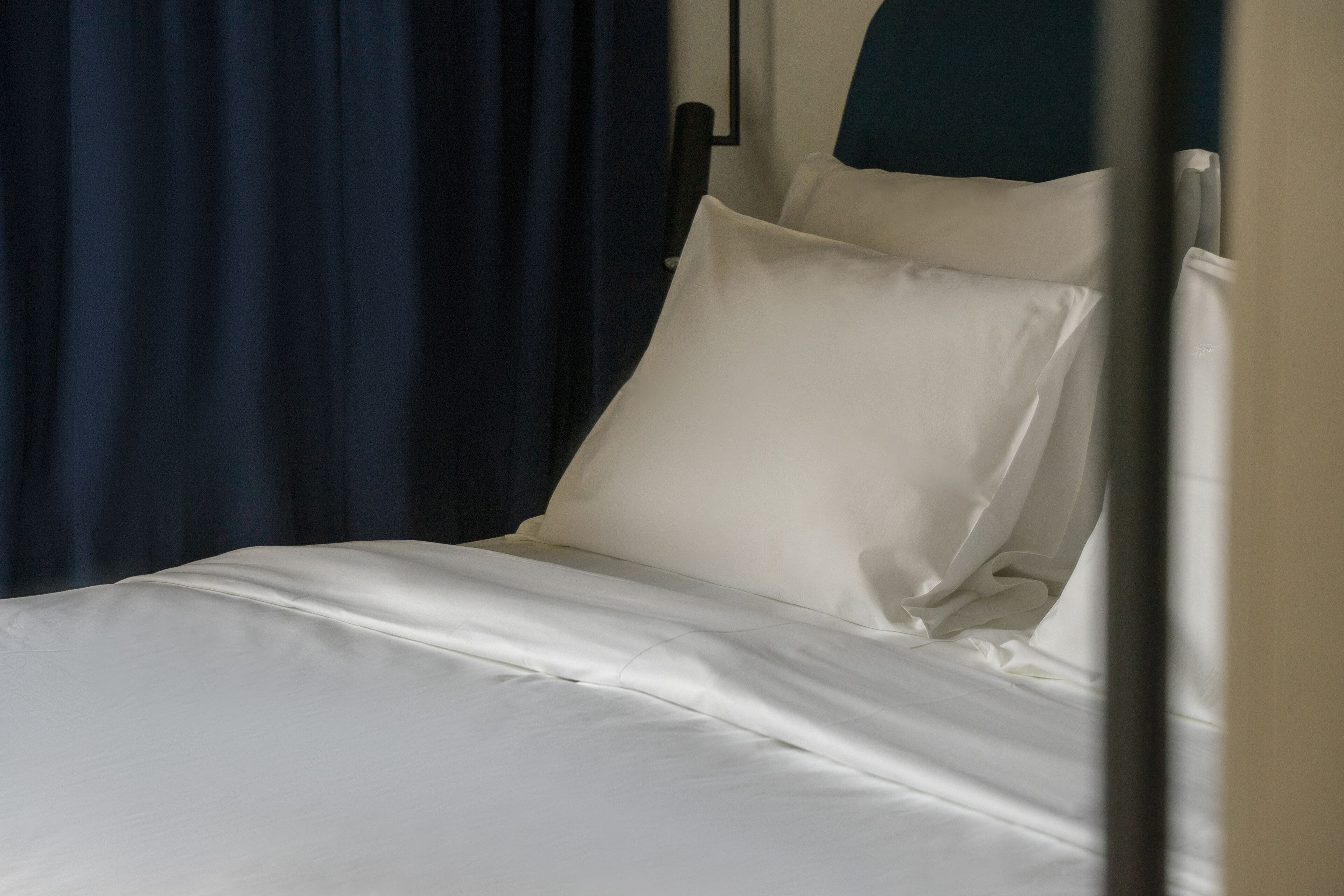 Un lit avec du linge de lit blanc et un rideau bleu foncé en arrière-plan.