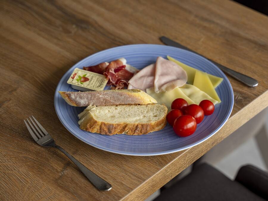En tallerken med brød, ost, tomater og lufttørret kød på et træbord.