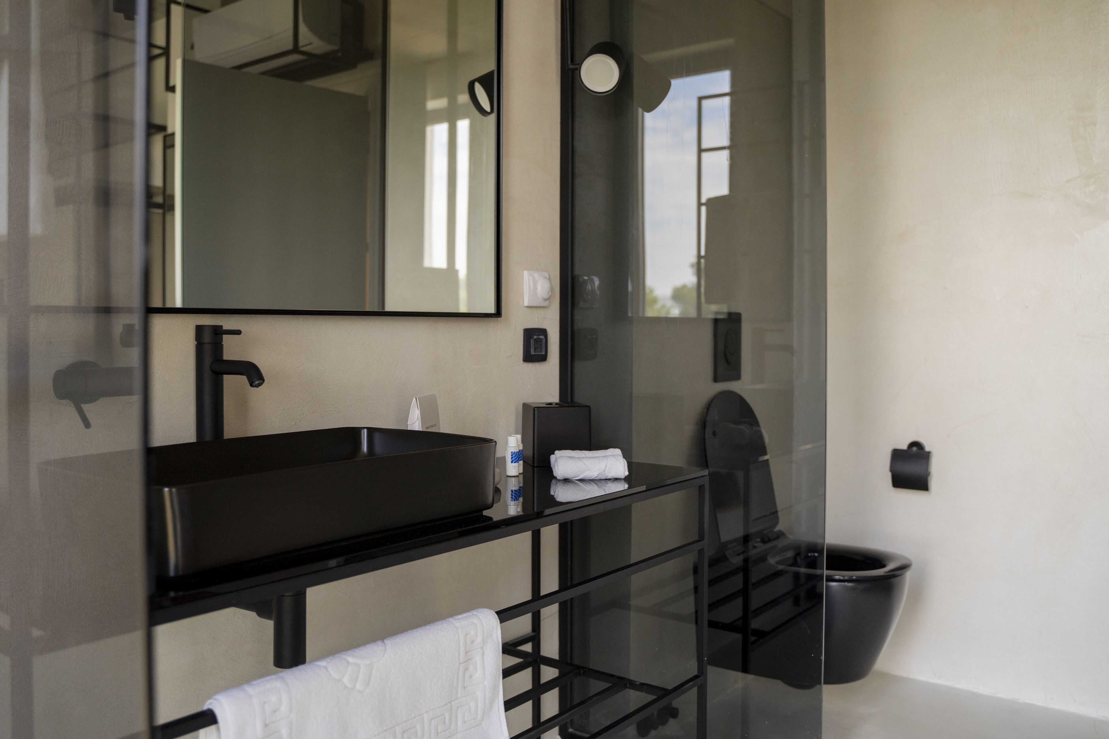 A modern bathroom with a black sink, a mirror, a towel rack, and a black toilet.