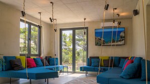 A modern living room with blue sofas, colorful cushions, and a large window with a view of trees and the sky. - Moro Inn  (Korcula)