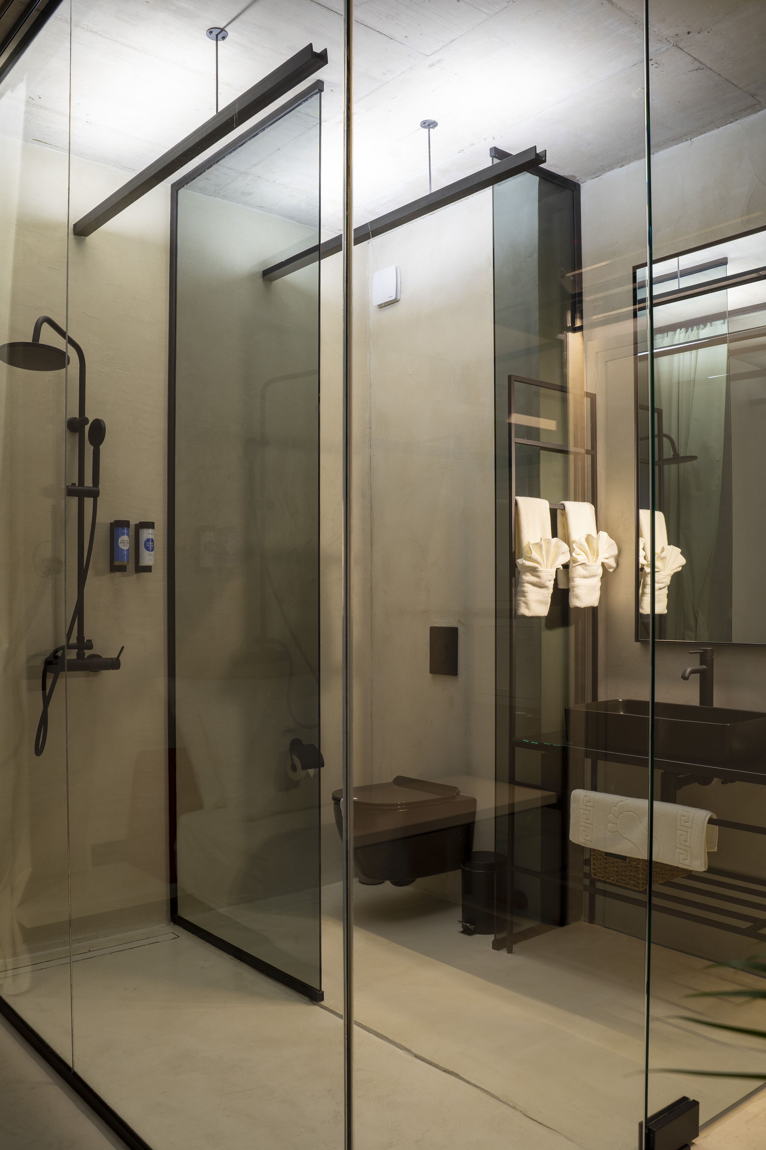 Un baño moderno con cabina de ducha de vidrio, un perchero con toallas y un lavabo con espejo.