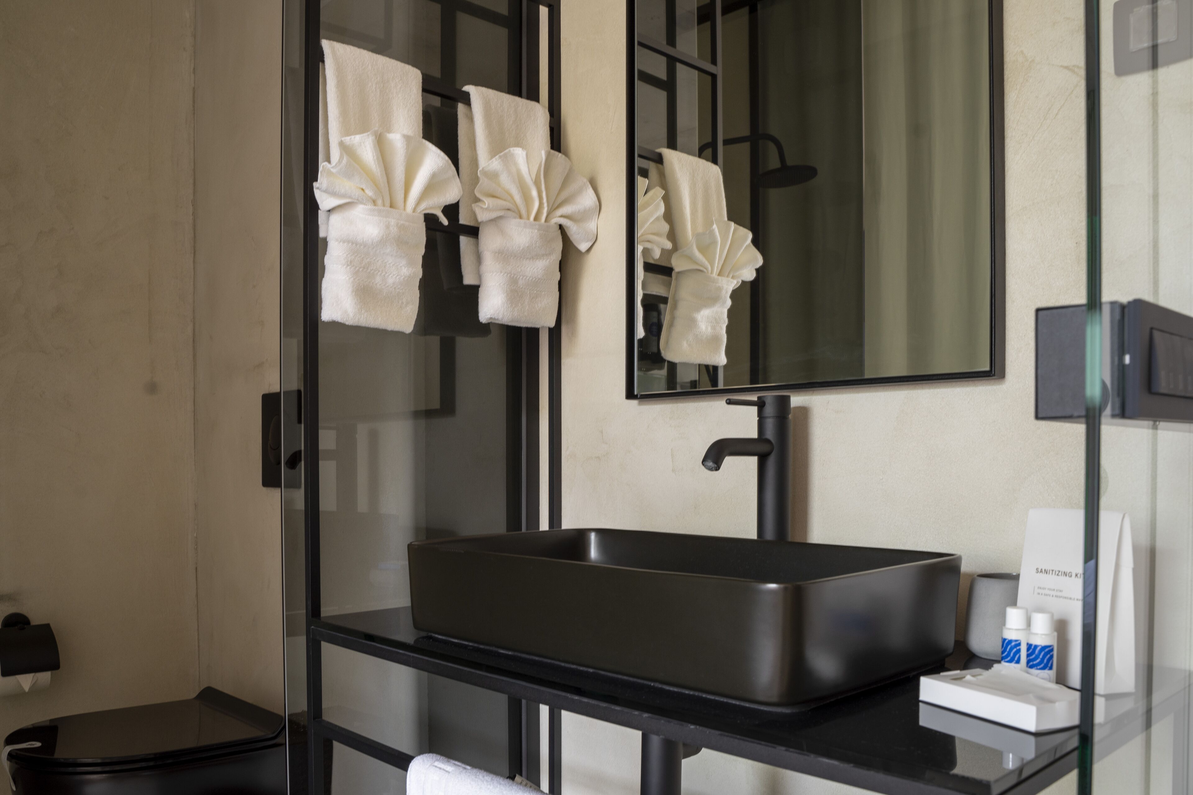 A modern bathroom with a black sink, a mirror, and two towels hanging on a towel rack.