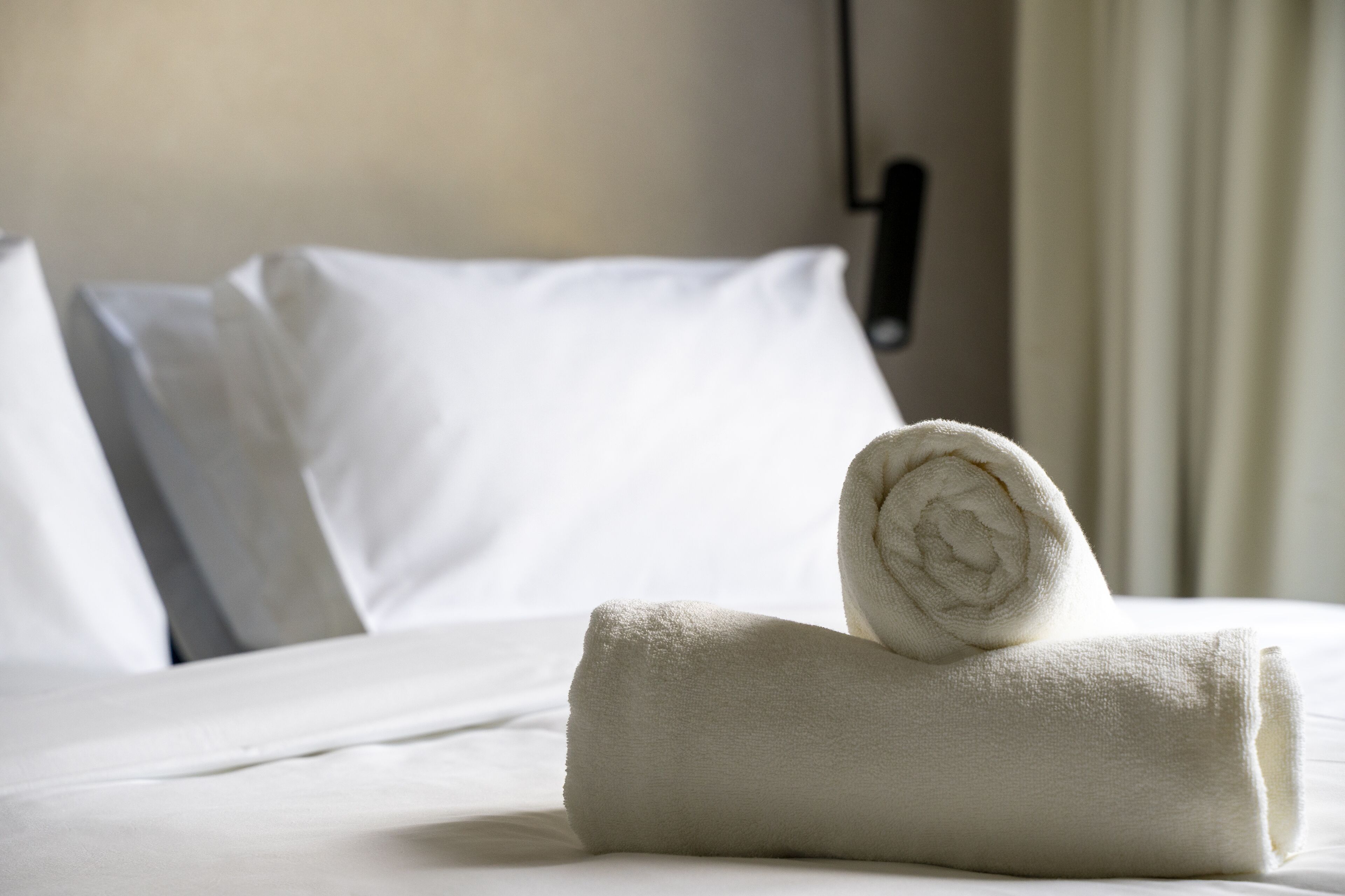 A neatly made bed with white linens and a rolled towel on top.