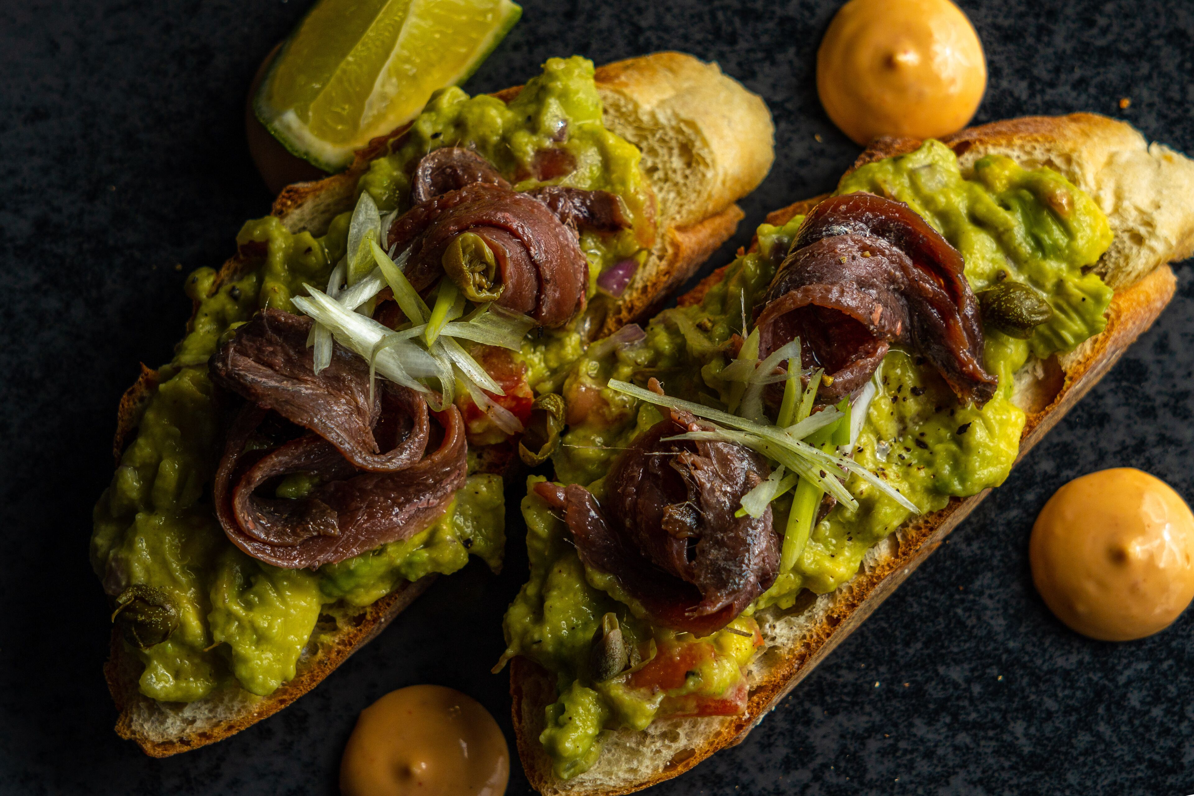Two pieces of bread topped with guacamole, bacon, and onions.