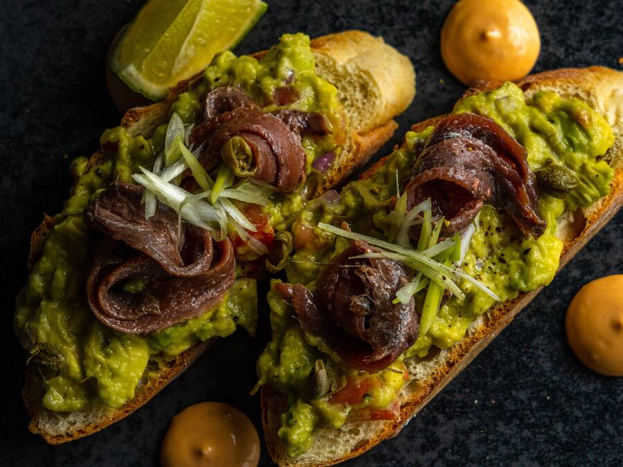 Two pieces of bread topped with guacamole, bacon, and onions.