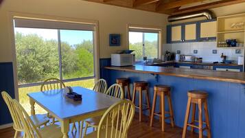 A kitchen with a large window, wooden bar stools, a table with chairs, and a microwave.