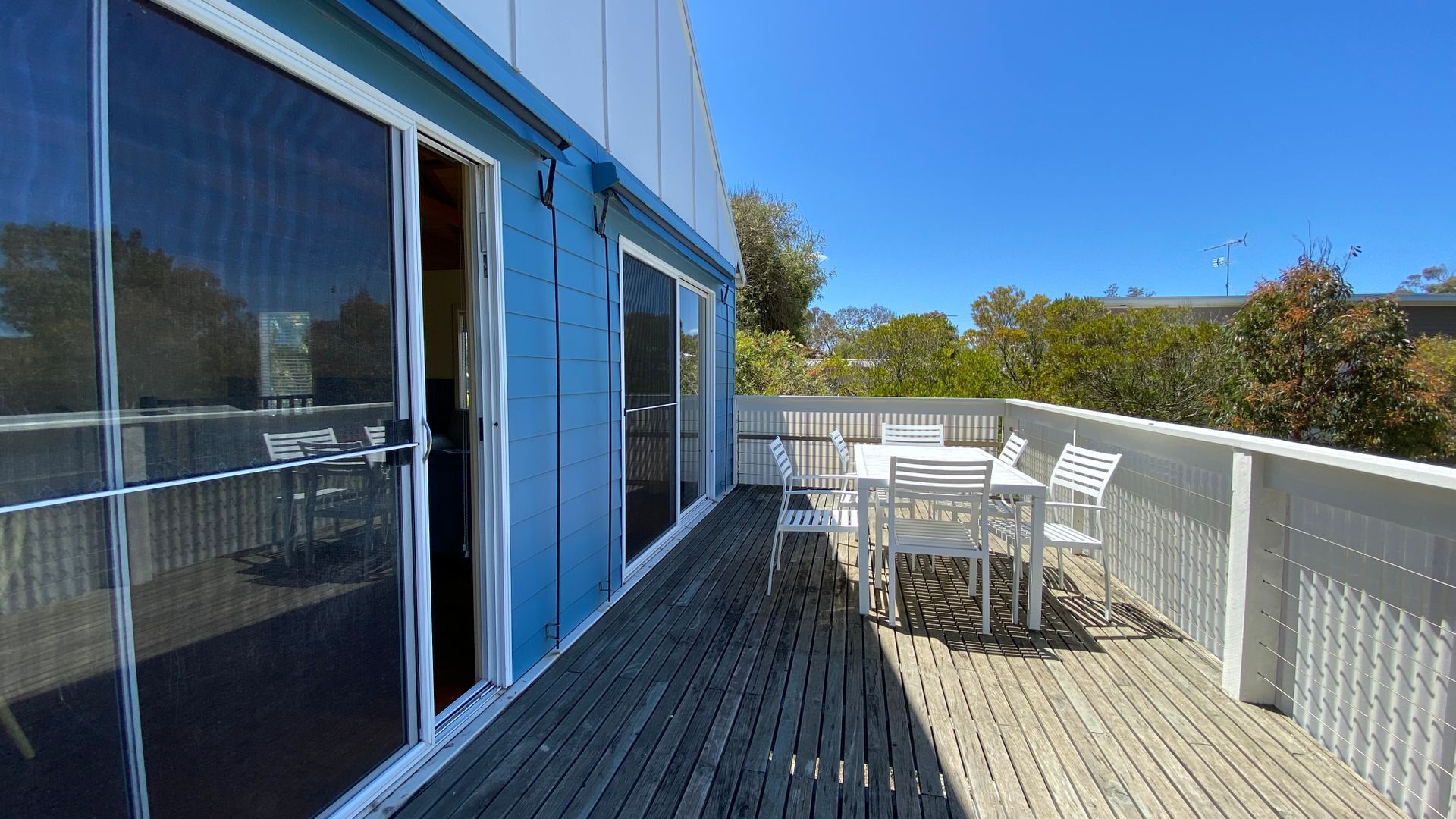 Une terrasse en bois avec une table et des chaises, une porte-fenêtre coulissante et une clôture blanche.