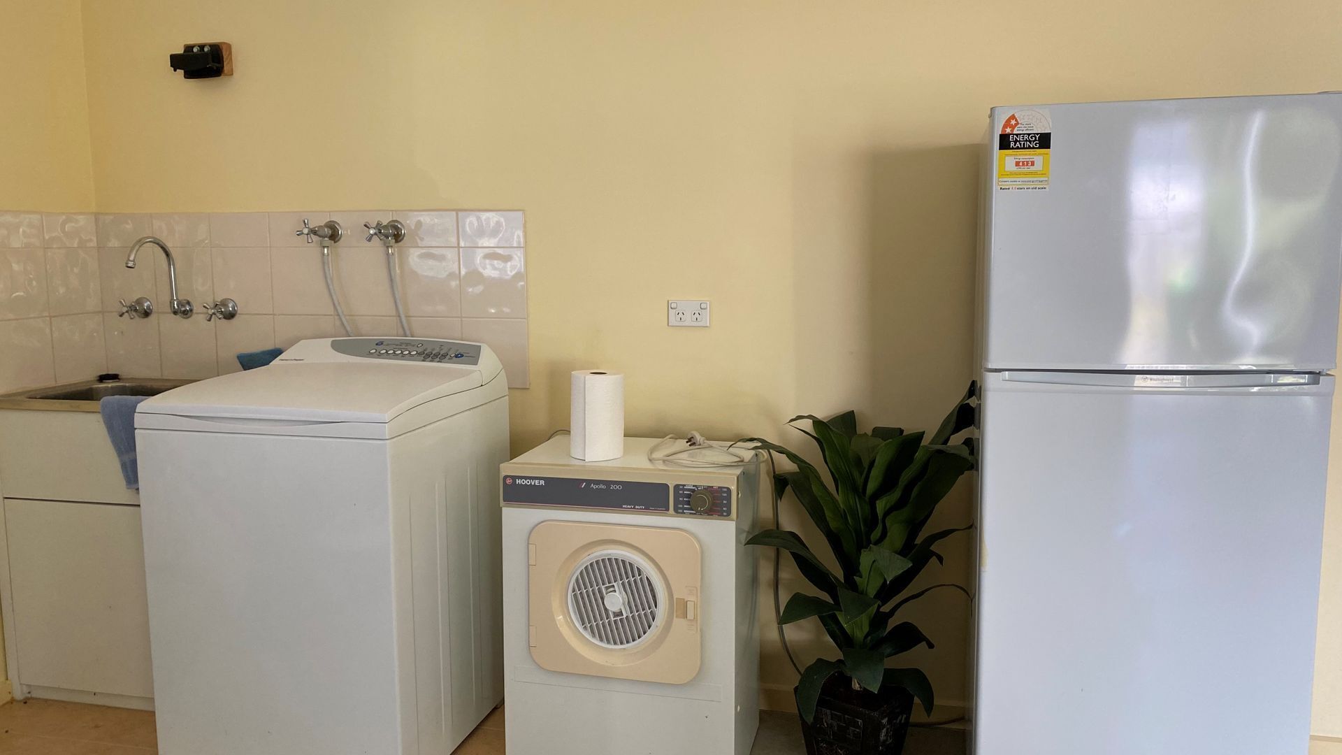 A compact kitchen with a washing machine, a dryer, a small heater, and a refrigerator.