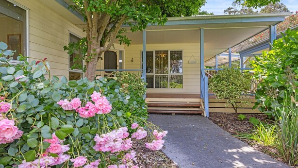 A building with a porch, a tree, and pink flowers in the foreground. - Surf Mist Retreat (Inverloch)