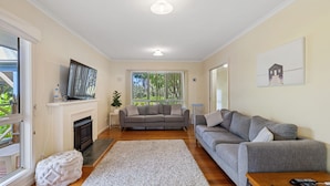 A living room with a fireplace, two sofas, a TV, and a painting on the wall. - Surf Mist Retreat (Inverloch)
