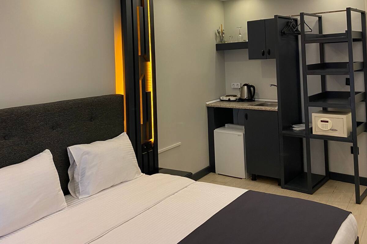 A modern hotel room with a large bed, a small kitchenette, and built-in shelving.