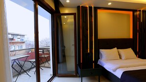 A modern hotel room with a large bed, a glass door leading to a balcony, and a view of the cityscape. - Galata King Suites (Istanbul)