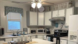 A kitchen with a central island, two bar stools, a ceiling fan, and white cabinetry. - 4 Bedroom Comfortable Cottage (Versailles)