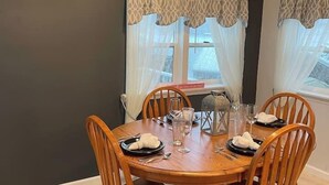 A dining area with a round wooden table, four wooden chairs, and a window with patterned curtains. - 4 Bedroom Comfortable Cottage (Versailles)