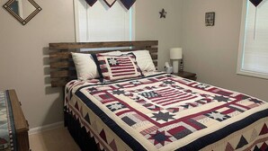 A bedroom with a wooden headboard, a quilted bedspread, a bedside table, and a nightstand. - 4 Bedroom Comfortable Cottage (Versailles)