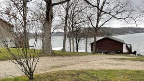 A lakeside cabin with a gravel path leading to it, surrounded by leafless trees and a view of the lake. - 4 Bedroom Comfortable Cottage (Versailles)