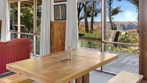Una mesa de madera con bancos en una terraza, con vista a árboles y colinas.