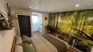 A bedroom with a bed, a wardrobe, a door leading to a balcony, and a forest mural on the wall.