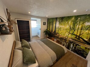 A bedroom with a bed, a wardrobe, a door leading to a balcony, and a forest mural on the wall.