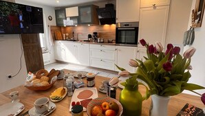 A modern kitchen with white cabinets, a built-in oven, and a television mounted on the wall.
