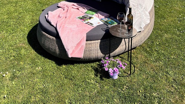 A cozy outdoor sleeping area with a canopy, a cushioned bench, a small table with a bottle and glass, and a pink blanket.
