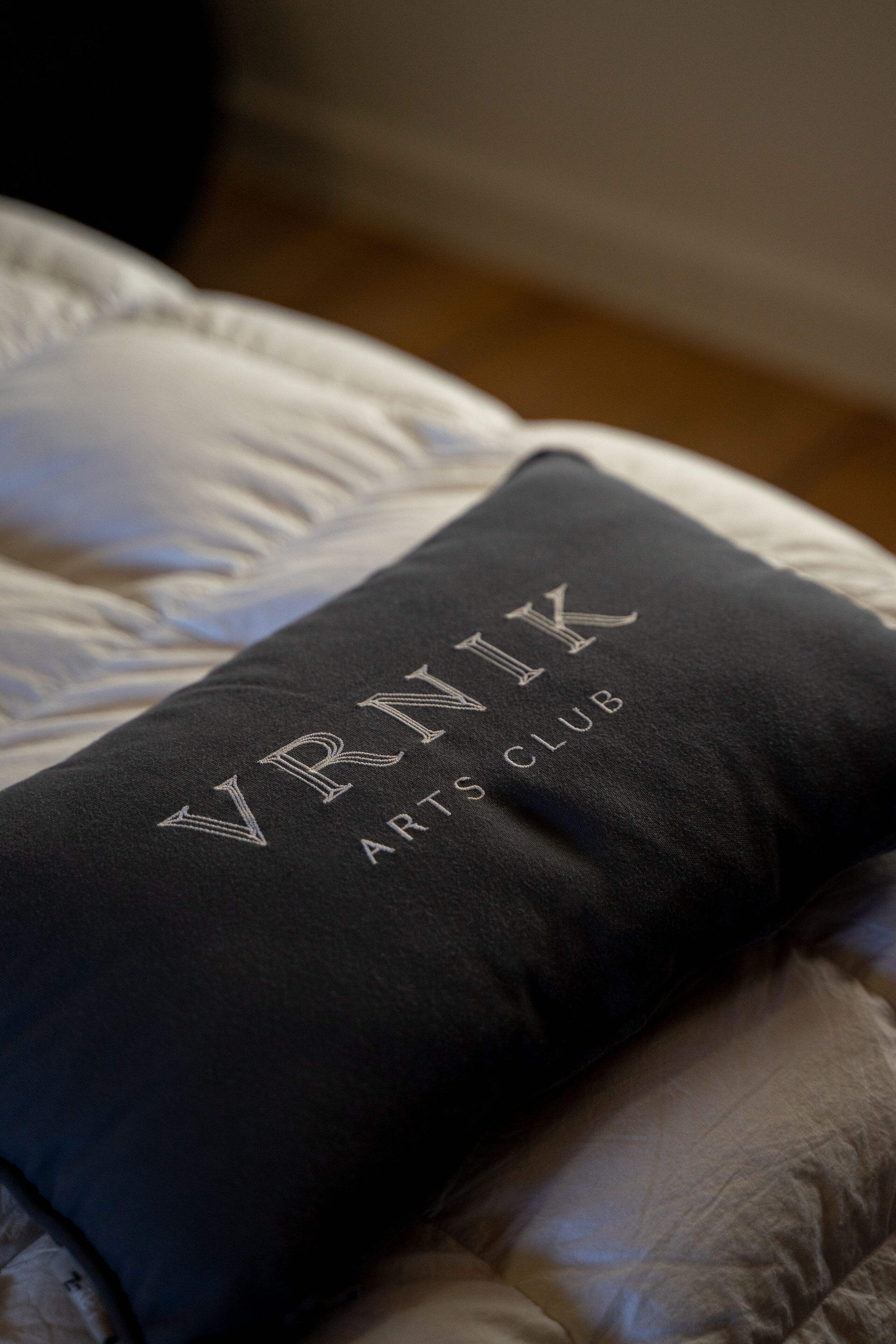 A pillow with embroidered text "VINK ARTS CLUB" on a bed.