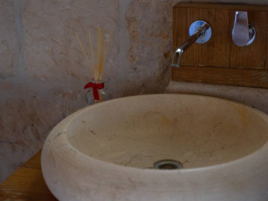 Un lavamanos de cerámica beige y forma redonda, con encimera de madera, un grifo metálico y un pequeño jarrón con cañas.