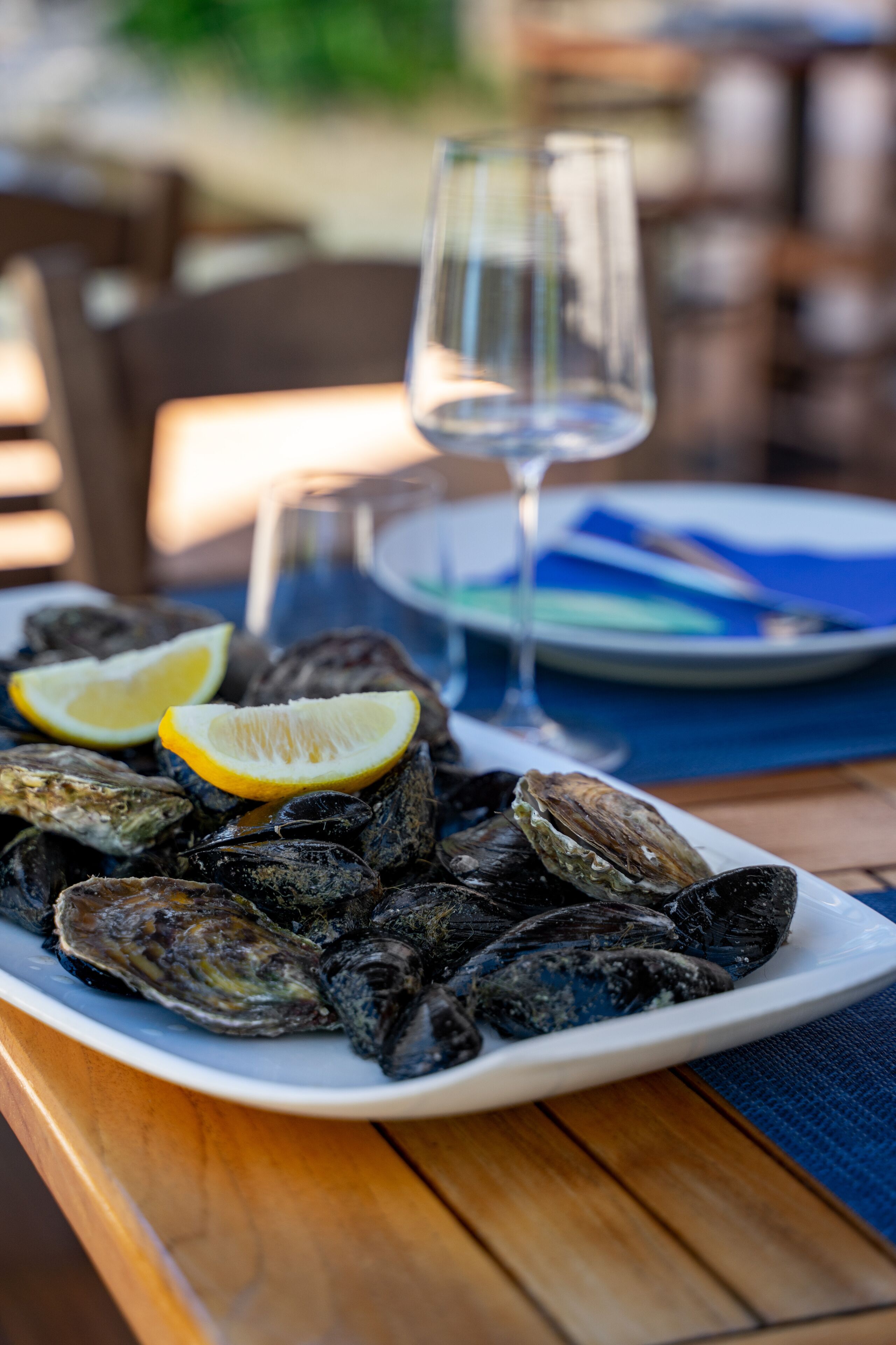 A plate of oysters with lemon wedges on a wooden table, a glass of water, and a blue napkin.