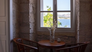 Una habitación rústica con pared de piedra, una mesa de madera, dos sillas y una ventana con vistas al mar.