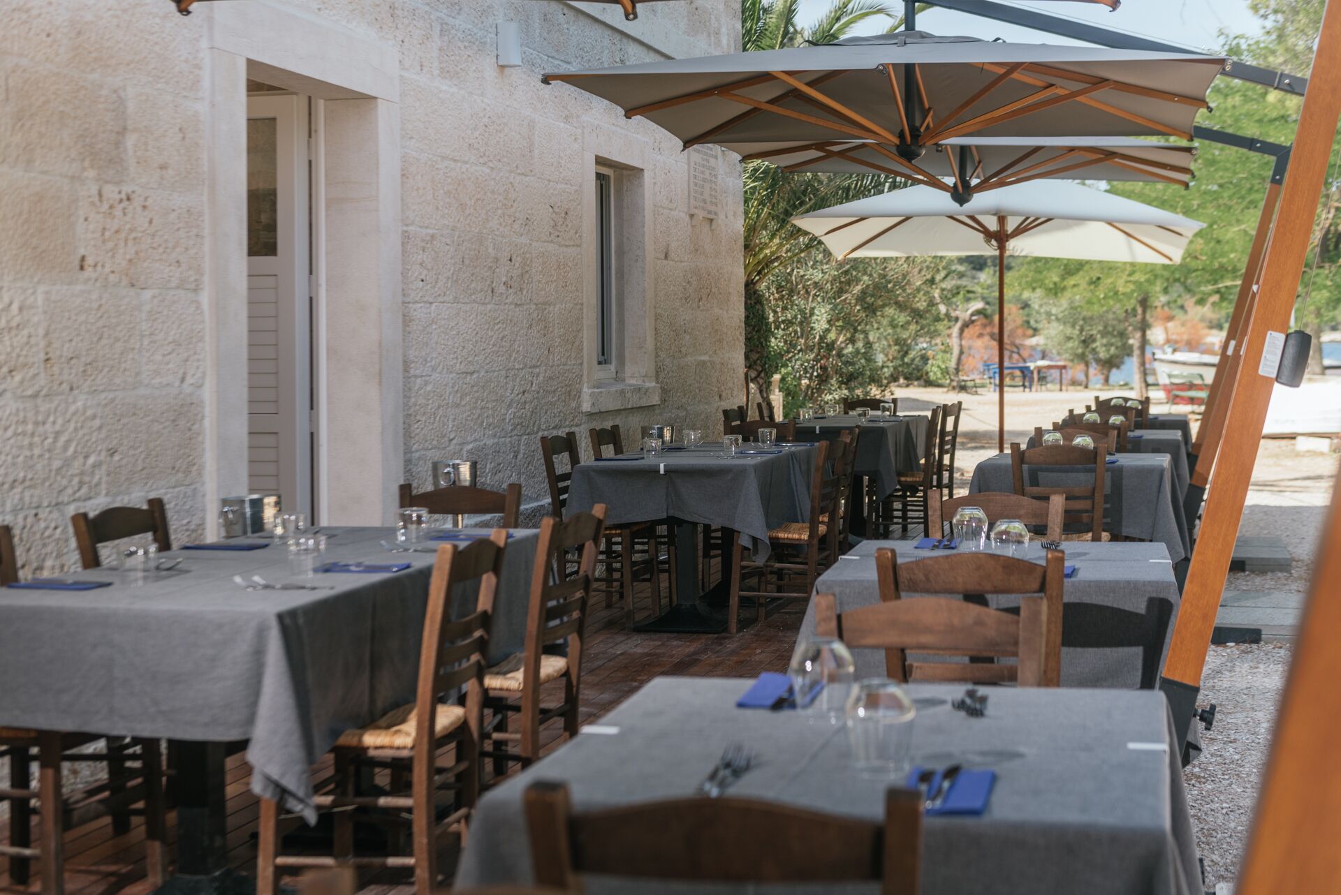 An outdoor dining area with tables and chairs, umbrellas, and a stone building in the background.