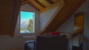 Un dormitorio con techo inclinado, una cama, un escritorio y una ventana con vistas a la montaña.