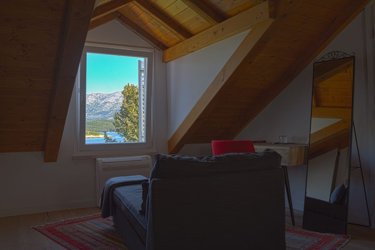 A bedroom with a sloped ceiling, a bed, a desk, and a window with a mountain view.