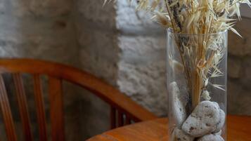 A clear glass vase with dried plants and smooth stones on a wooden table.