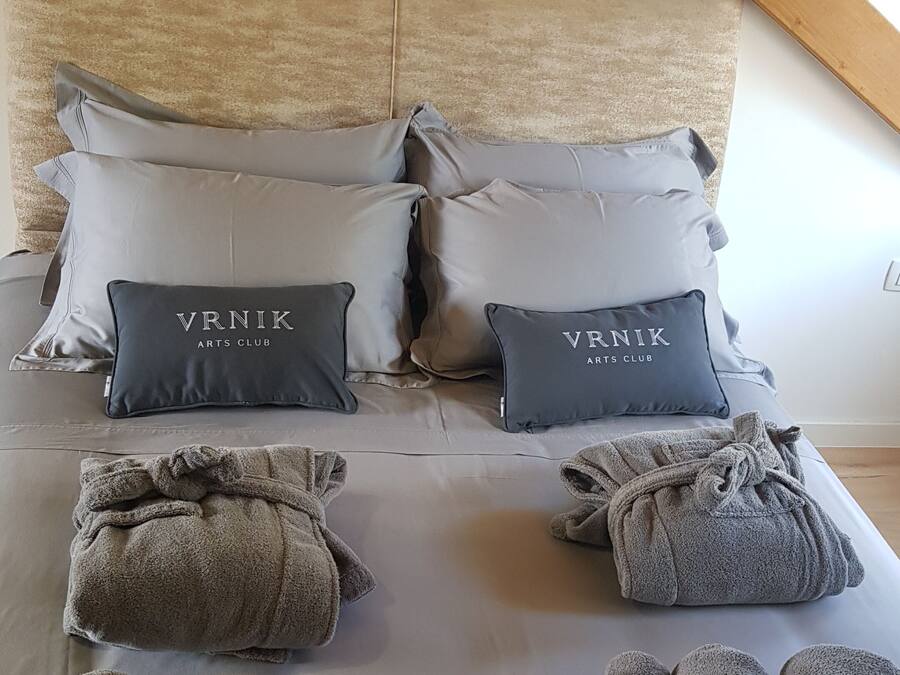A neatly made bed with grey towels and pillows labeled "VNRIK ARTS CLUB".