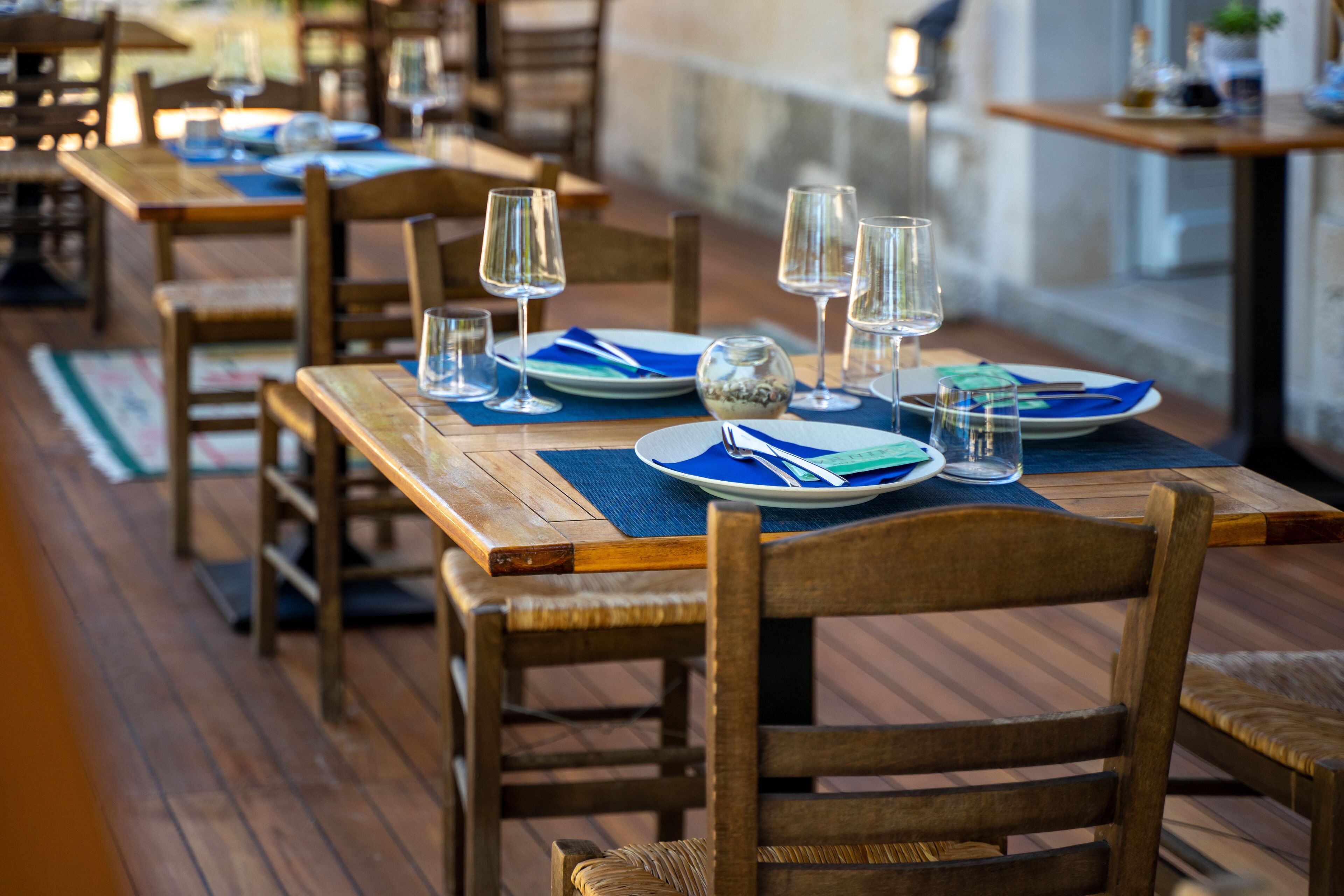 Un restaurante con mesas y sillas de madera, con platos, vasos y cubiertos colocados.