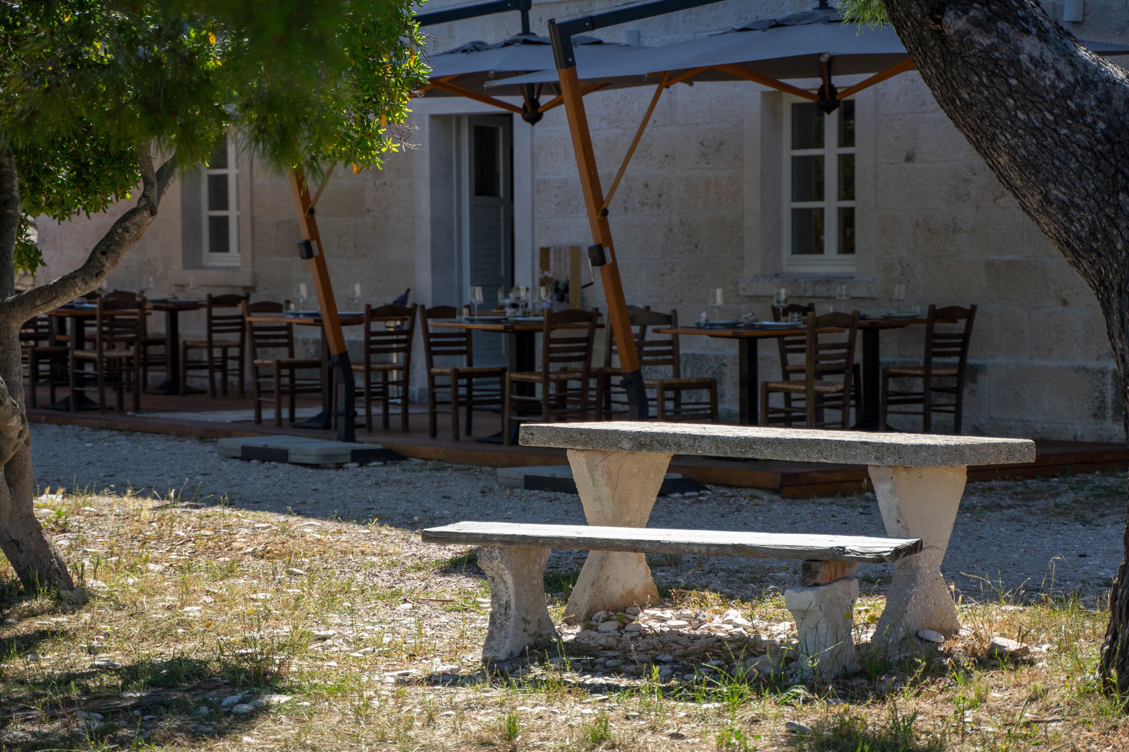 Un área de comedor al aire libre con mesas y sillas de piedra, una pérgola y un edificio al fondo.