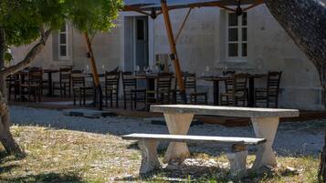 Un área de comedor al aire libre con mesas y sillas de piedra, una pérgola y un edificio al fondo.